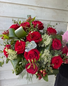 A stunning bouquet of 12 red roses with berries and mixed foliage presented in a gift box in water.